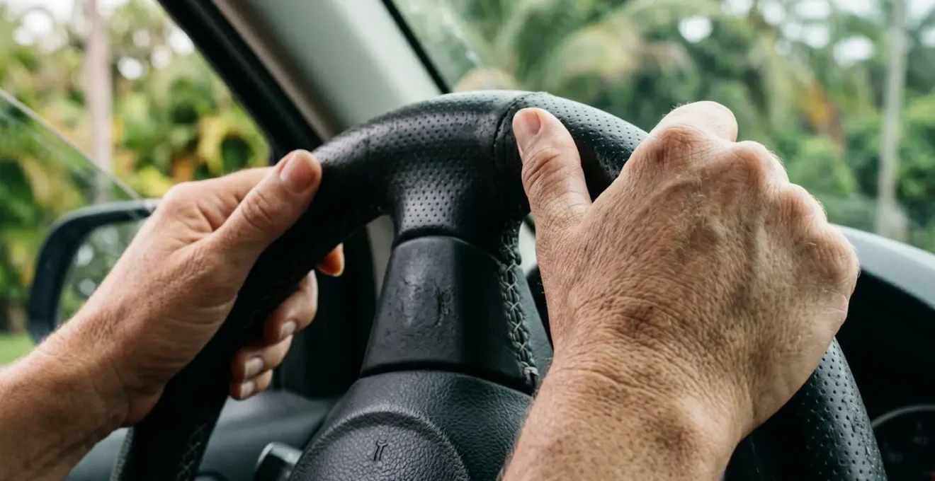 Gros plan macro sur des mains tenant un volant de voiture, lumière naturelle douce, végétation tropicale floue en arrière-plan